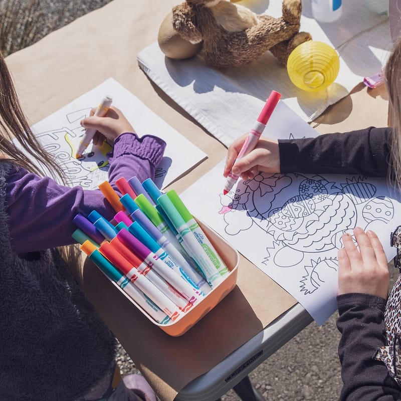 two young girls sitting at a table with markers and crayons